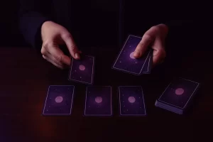 Manos barajando y colocando cartas de tarot con fondo violeta estrellado sobre una mesa oscura, símbolo de introspección y guía espiritual.