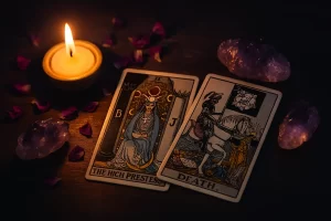 Cartas del tarot La Sacerdotisa y La Muerte iluminadas por una vela, rodeadas de pétalos y amatistas, símbolo de introspección y transformación espiritual.